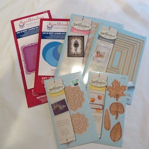 Puede incluir: Un conjunto de troqueles Nestabilities de Spellbinders en varias formas y diseños. Los conjuntos incluyen marcos decorativos, círculos y formas de hojas. El embalaje es rojo, azul y beige, con el logotipo de Spellbinders.