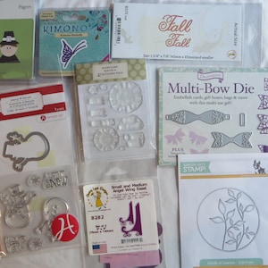 May include: Assortment of craft dies for paper crafting. The dies include a pilgrim, a kimono, a butterfly, a snowman, a circle of leaves, and a variety of bows. The dies are silver and come in a variety of sizes.  SIMON SAYS STAMP! is printed on one of the dies.