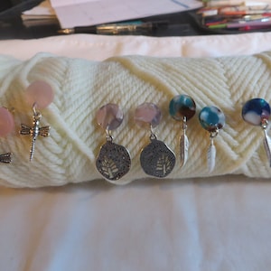 May include: Six pairs of colorful glass bead and metal charm earrings. The charms include a dragonfly, a leaf, and a feather.