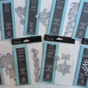 May include: A collection of Memory Box steel craft dies, each packaged in a clear plastic sleeve with a blue and white backing. The dies feature intricate designs, including snowflakes, borders, and floral elements, suitable for cardstock, felt, and fabric.