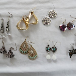 May include: Assortment of earrings in various styles and colors, including silver, gold, and purple. Some earrings feature intricate designs, while others are simple and elegant.