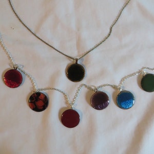 May include: Six round pendants on silver chains, each with a different colored resin design. The pendants are black, red, orange, purple, blue, and green.