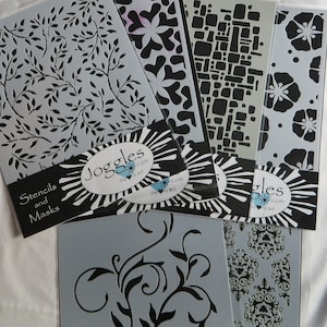 May include: A set of six black and white stencils for crafting and decorating. The stencils feature various designs, including floral, geometric, and abstract patterns. The stencils are packaged with a black and white label that reads "Stencils and Masks" and "Joggles the art of art.com".