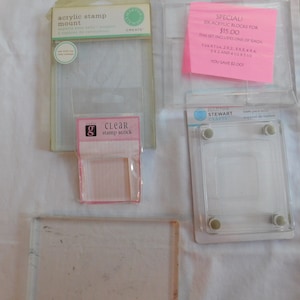 Puede incluir: Un conjunto de seis bloques de sellos de acr&iacute;lico transparente de diferentes tama&ntilde;os, empaquetados en una bolsa de pl&aacute;stico transparente con una etiqueta rosa que dice "SPECIAL! SIX ACRYLIC BLOCKS FOR $15.00 THIS SET INCLUDES ONE OF EACH 1X1, 1X2, 2X2, 3X4, 4X4, 5X2 AND 4X2, 5X2, 5X5 YOU SAVE $2.00". Tambi&eacute;n hay dos soportes de sellos de acr&iacute;lico transparente, uno con una etiqueta rosa que dice "CLEAR stamp stock" y el otro con una etiqueta blanca que dice "acrylic stamp mount".