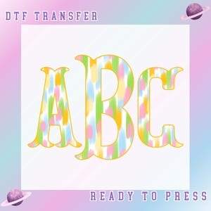 May include: DTF transfer design featuring the letters ABC in a colorful, watercolor-style pattern with yellow outlines. The design includes pastel shades of pink, green, blue, and yellow. The words "DTF TRANSFER" and "READY TO PRESS" are also visible.