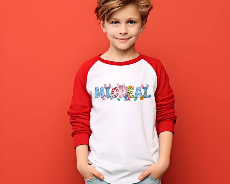 May include: A white and red raglan-style shirt with the name "MICHAEL" printed across the chest in colorful, cartoon-style letters. The letters are decorated with various cartoon characters and objects.