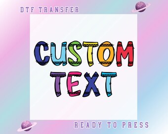May include: A white background with the words "CUSTOM TEXT" in large, colorful, outlined letters. The text is in a playful font with a black outline and filled with blue, green, yellow, orange, red, and purple. The words "DTF TRANSFER" and "READY TO PRESS" are above and below the main text.