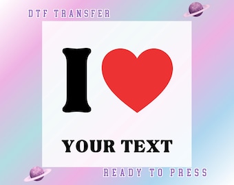 May include: A DTF transfer design featuring a black letter "I" next to a red heart, with the words "YOUR TEXT" in bold black font. The design is set against a white background with a pastel gradient. The text "READY TO PRESS" is also included.