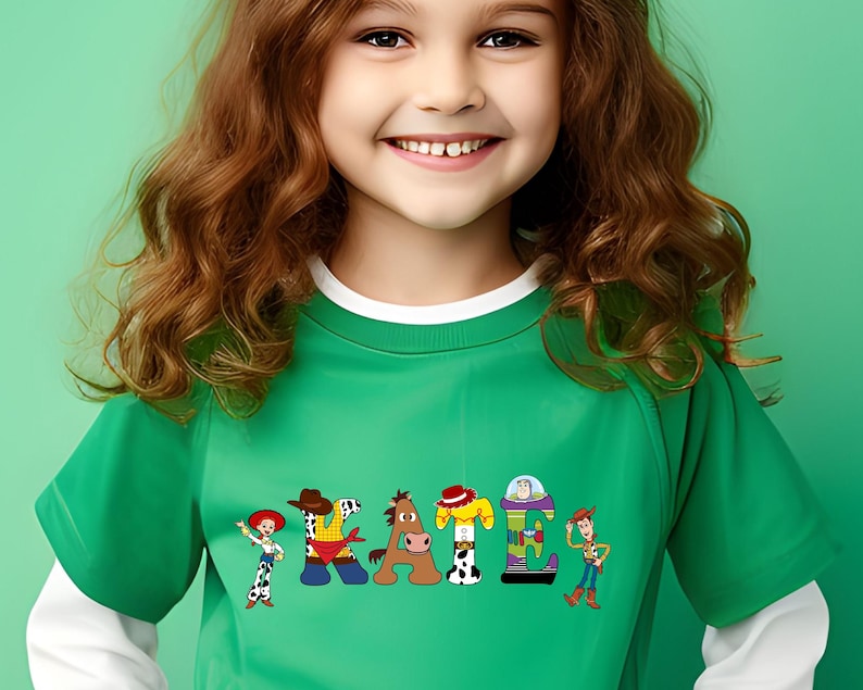 May include: A green t-shirt with white trim featuring the word "PEACE" spelled out with cartoon characters. The characters are from the Toy Story franchise. The shirt is worn by a young girl with long brown hair.