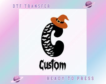 May include: A black letter "C" design with a witch hat and bats, with the word "Custom" in a spooky font. The design is a DTF transfer, ready to press. The background is a gradient of pink, purple, and blue.