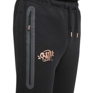 Puede incluir: Pantalones deportivos negros con cremallera y detalles de cord&oacute;n en oro rosa. Un logotipo en oro rosa est&aacute; impreso en la pierna izquierda. Los pantalones tienen un corte ajustado y est&aacute;n hechos de un material suave.