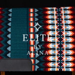 Könnte beinhalten: Türkisfarbene Satteldecke mit geometrischem Muster in Orange, Weiß und Burgunderrot. Sie hat eine schwarze Lederbasis. Der Text "ELITE BY ALINA" ist weiß dargestellt. Für den Reitsport konzipiert.