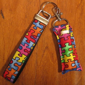 May include: A colorful puzzle piece patterned key chain with a black zipper and a matching puzzle piece patterned fabric pouch with a silver key ring.