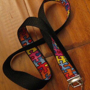 May include: A black lanyard with a colorful puzzle piece pattern. The lanyard has a silver key ring attached.