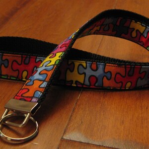 May include: A black and multi-colored key chain with a puzzle piece pattern. The key chain has a silver key ring.