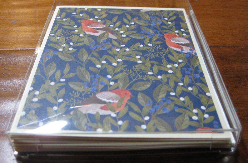 May include: A stack of blank greeting cards with a blue background and a repeating pattern of white berries, green leaves, and red birds. The cards are packaged in a clear plastic sleeve.