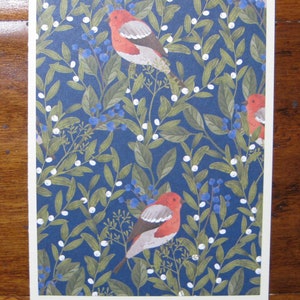 May include: A blue background with a repeating pattern of white berries, green leaves, and red birds. The birds have white markings on their wings and are perched on the branches.