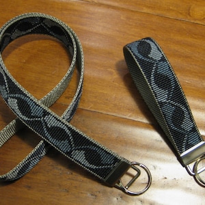 Puede incluir: Un llavero de tejido tejido con un patrón negro y gris y un anillo de llave plateado.