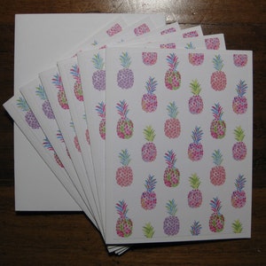 Könnte beinhalten: Ein Stapel von acht leeren weißen Karten mit einem sich wiederholenden Muster aus rosa, lila und grünen Ananas. Die Ananas bestehen aus kleinen Punkten und haben einen Aquarell-Effekt.