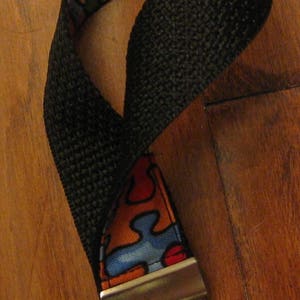 May include: A black and colorful key chain with a metal ring and a clasp. The colorful part of the key chain has a puzzle piece design with red, blue, yellow, and green colors.