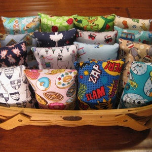 May include: A basket filled with colorful fabric squares, each with a different design. The designs include a cartoon pig, a llama, donuts, a comic book theme, and a cartoon character.