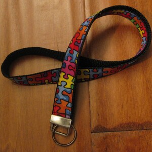 May include: A black and colorful puzzle piece patterned lanyard with a silver key ring.