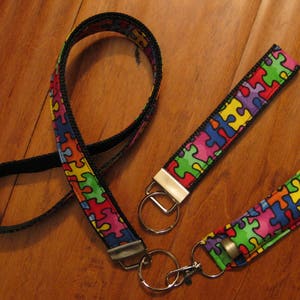 May include: A colorful puzzle piece patterned lanyard with a black strap and matching key chain. The lanyard has a silver swivel clip and a silver key ring.