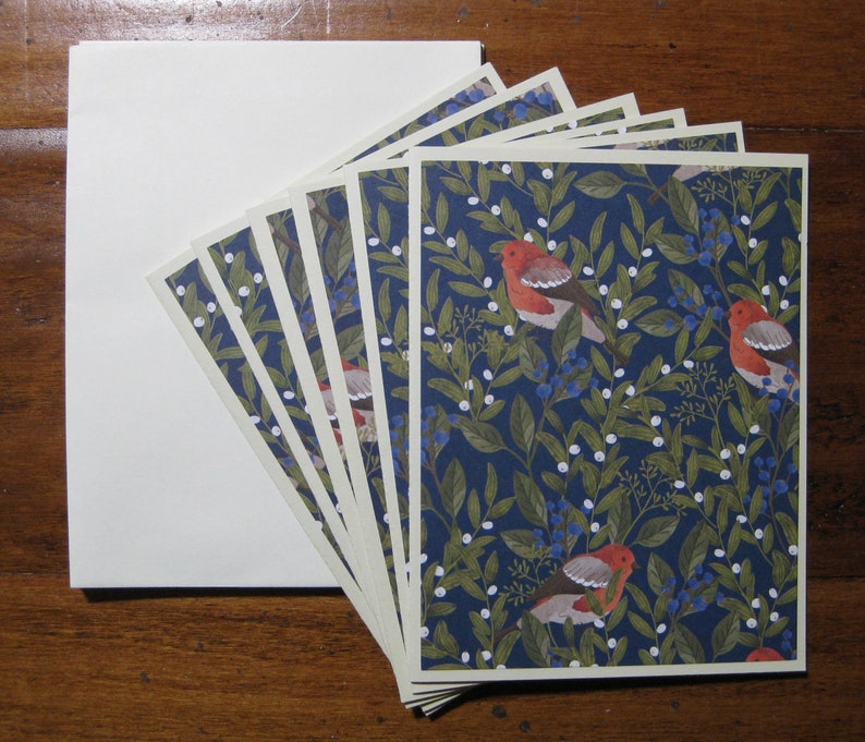 May include: A set of six blank greeting cards with a blue, white, and red floral pattern featuring birds. The cards have a cream-colored border.