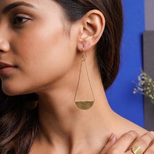 Puede incluir: Pendientes geométricos dorados, con un diseño triangular y una base semicircular. Los pendientes cuelgan de un gancho y se llevan en la oreja. La joya es un accesorio sencillo pero elegante.