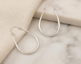 May include: A pair of silver-toned teardrop-shaped hoop earrings with a smooth, polished finish. Each earring features a thin, continuous metal wire frame that tapers to a point at the top, secured by a simple hinged closure mechanism.