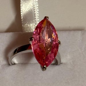 May include: A silver ring with a large, marquise-shaped pink gemstone. The gemstone is multi-faceted, catching the light. The ring has a simple, polished silver band, offering a classic and elegant appearance.