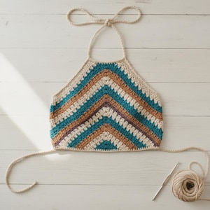 May include: A handmade crochet halter top in a chevron pattern. The top features alternating stripes of teal, tan, brown, and cream colors. The halter top has a tie closure at the neck and back. A ball of yarn and a crochet hook are also visible.