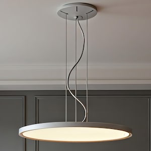 Puede incluir: Una lámpara colgante moderna y minimalista. Tiene un diseño circular y plano que emite una luz cálida. Se suspende del techo mediante finos cables y un cable negro curvado. La lámpara es de color gris neutro y tiene un diámetro de unos 60 cm.