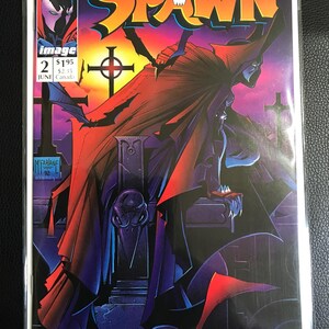 May include: Spawn comic book cover showing a figure in a red cape against a sunset. The title "SPAWN" is in large, stylized letters. The comic book is issue number 2, with the Image Comics logo and the name "SIMMONS".