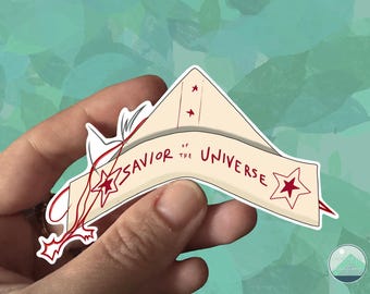 May include: A sticker featuring a cream-colored banner with the text "Savior of the Universe" in red. The banner has red star accents and is held by a hand against a teal and green background.