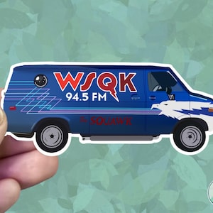 May include: A sticker depicting a blue van with the text "WSQK 94.5 FM" in red and white. The van has a white eagle graphic and the words "The SQUAWK" in red. The sticker is held by a hand.