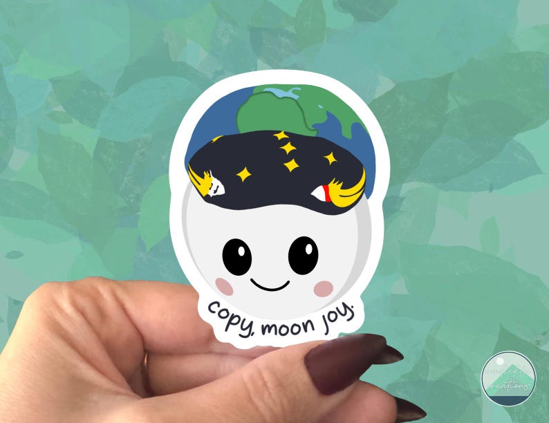 May include: A white sticker with a cartoon moon character wearing a dark blue hat with yellow stars and a green and blue earth on top. The sticker has the text "copy, moon joy."