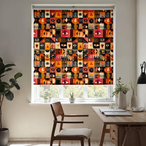 Puede incluir: Una persiana enrollable estampada con un diseño geométrico repetido que incorpora ojos, formas y motivos florales en tonos rojos, naranjas, negros y crema. La persiana está instalada en una ventana, con una silla y un escritorio de madera visibles.