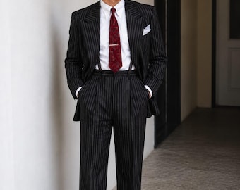 May include: A black pinstripe suit featuring a white dress shirt, a dark red patterned necktie with a gold tie bar, and a white pocket square. The trousers are high-waisted with pleats and cuffs, worn with brown leather dress shoes.