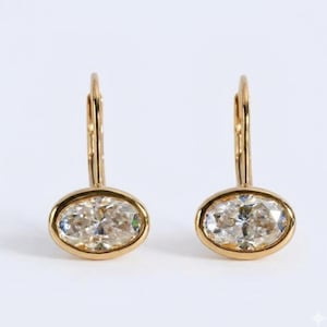Pode incluir: Um par de brincos de ouro com fecho de alavanca, apresentando pedras ovais facetadas e transparentes em engastes de ouro polido. Os brincos possuem um mecanismo de fio vertical simples para uma fixação segura e acabamento brilhante.