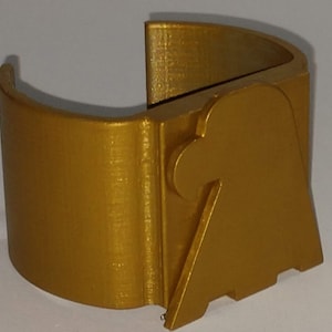 May include: A gold-colored, curved, 3D-printed object with a unique design. The object has a rounded, open shape with a connecting piece and a notched base. The overall design is geometric and modern.