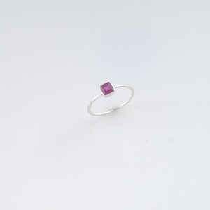 Peut inclure: Une fine bague en argent dotée d'une petite pierre précieuse magenta de taille carrée, fixée dans un sertissage métallique simple. La bague présente une finition lisse et polie, offrant une apparence délicate avec une pierre rose-rouge vive.