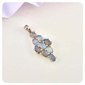 Pode incluir: Um pendente de prata com um grupo de pedras ovais de labradorite. As pedras exibem tons de azul, cinza e iridescentes. O pendente tem um design simples e elegante, adequado para uso diário ou ocasiões especiais.