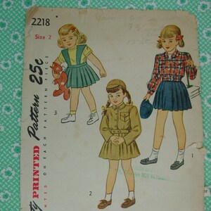 May include: Vintage Simplicity sewing pattern for girls' dresses. The pattern is for sizes 2 and includes three different dress styles: a plaid shirt dress, a safari-style dress, and a pinafore dress. The pattern is printed on a single sheet of paper and includes instructions for sewing the dresses.