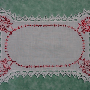 May include: White crocheted doily with a red embroidered floral design. The doily has a scalloped edge and is perfect for adding a touch of elegance to any table setting.