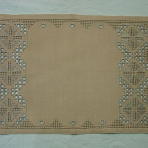 May include: Tan rectangular placemat with intricate embroidered geometric patterns in the corners and along the edges. The embroidery is in a darker shade of tan, creating a contrast. The placemat is made of a woven fabric.