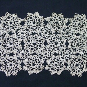 May include: An off-white, rectangular doily featuring an intricate, repeating floral lace pattern created with fine thread. The delicate, openwork design consists of interconnected circular motifs with scalloped edges, forming a symmetrical grid.