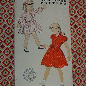 May include: Vintage New York Pattern 1224, size 2, featuring illustrations of two little girls in dresses. One dress is white with a red floral print, and the other is red with white polka dots. The pattern includes a "Gold Seal Guaranteed Perfect" seal.