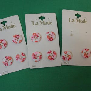 May include: Three cards of La Mode brand buttons. Each card holds two or three round buttons with a white background and a floral pattern in pink, orange, and brown. The cards are on a green surface.