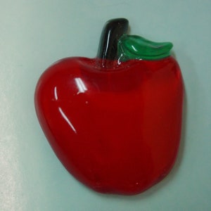 May include: A red glass apple with a green leaf on top. The apple is shiny and has a smooth surface.